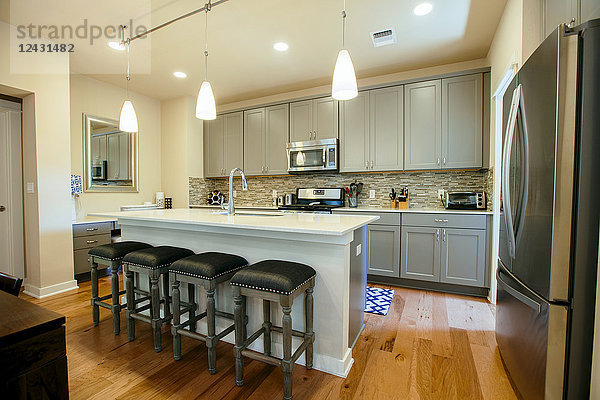 Moderne Wohnküche mit grün-grauen Einbauschränken  einer Kücheninsel mit hohen Barhockern und Holzfußboden.