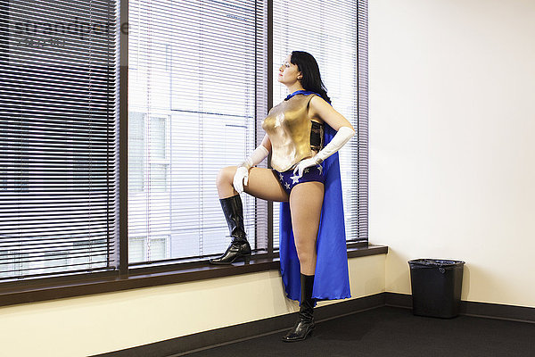 Eine Superheldin aus dem Büro einer kaukasischen Frau steht am Fenster und grübelt über ihren nächsten Schritt nach.
