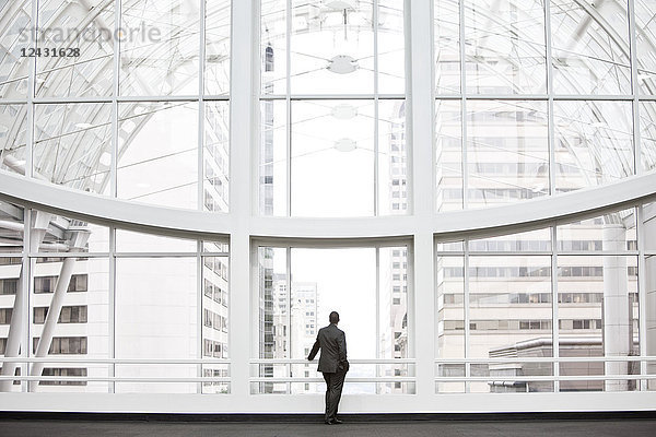 Ein Geschäftsmann in Silhouette  der an einem großen Fenster in der Lobby eines Kongresszentrums steht.