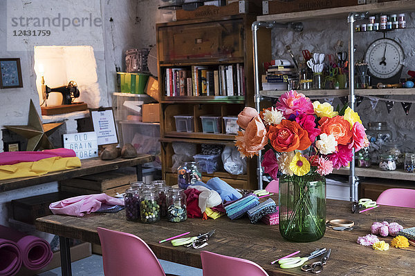 Ein Strauß bunter  handgefertigter Stoffblumen in einer Vase auf einem Tisch in einer Werkstatt.