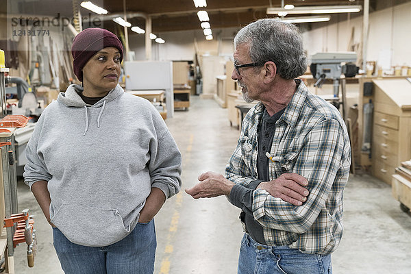 Ein älterer kaukasischer Zimmermann und eine schwarze Zimmermannsfrau diskutieren über ein Projekt in einer großen holzverarbeitenden Fabrik.