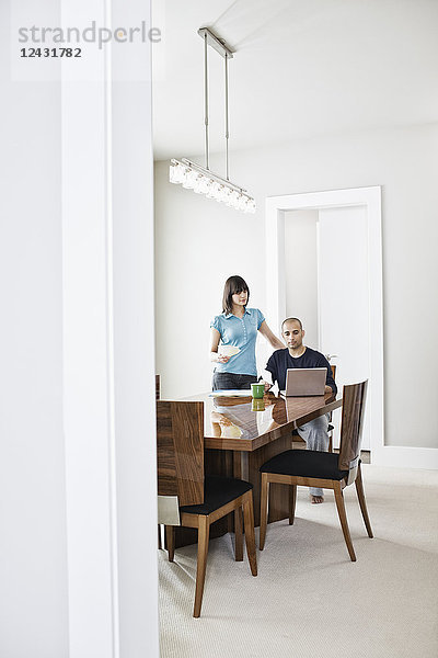 Ein spanischer Mann und eine Frau schauen auf einen Laptop-Computer auf dem Esstisch im Esszimmer eines neuen Zuhauses.