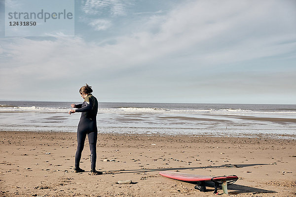 Mann trainiert  dehnt und wärmt sich vor dem Surfen an einem Sandstrand auf