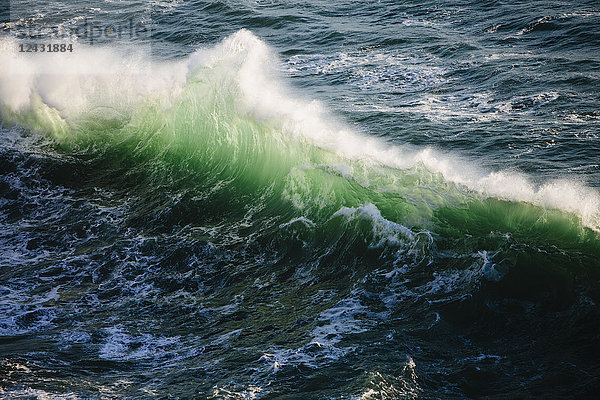 Eine weiße Brandungslinie mit grünen und türkisfarbenen Farben im Wasser. Wellen  die in der Abenddämmerung auf dem Ozean brechen.