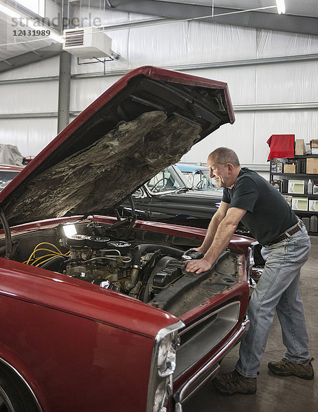 Ein älterer Automechaniker  der in seiner Werkstatt an einem Auto arbeitet.