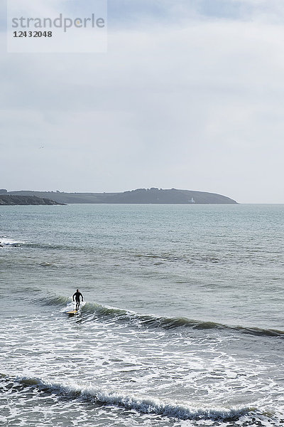 Surfer im Neoprenanzug reitet in Küstennähe auf der Meereswelle.