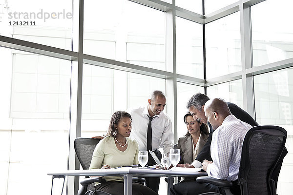 Eine gemischtrassige Gruppe von männlichen und weiblichen Geschäftsleuten bei einem Treffen an einem Konferenztisch neben einem großen Fenster in einem Kongresszentrum.