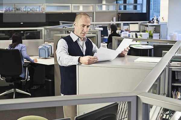 Kaukasischer Mann geht in Bürozellen den Papierkram durch.