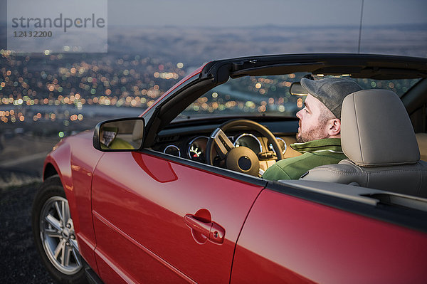 Ein kaukasischer Mann parkte in seinem Cabrio-Sportwagen und beobachtete den Sonnenuntergang über dem Clearwater River und der Stadt Lewiston Idaho.