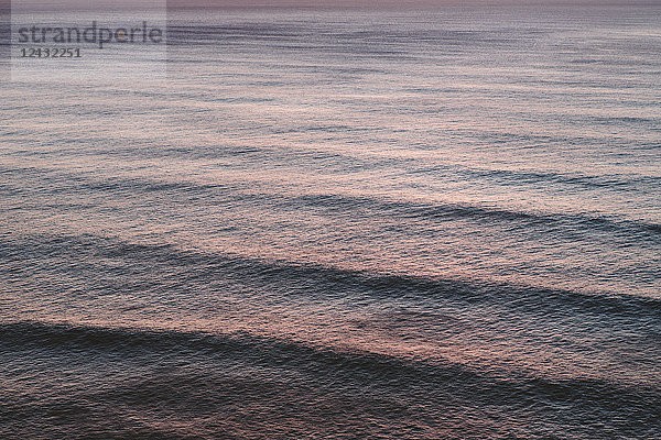 Blick von oben auf rollende Wellen  die zum Ufer vorrücken  ein Muster auf der Wasseroberfläche in der Abenddämmerung.