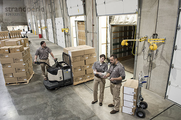 Ein Team von drei gemischtrassigen  uniformierten Lagerarbeitern  die in einem Vertriebslager verpackte Produkte hinten auf einen Lastwagen luden.