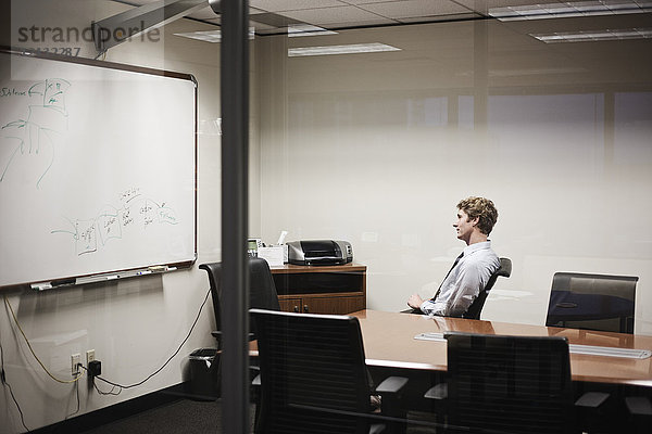 Blick durch Glas auf einen Geschäftsmann  der in einem Büro-Konferenzraum an einem Projekt arbeitet.