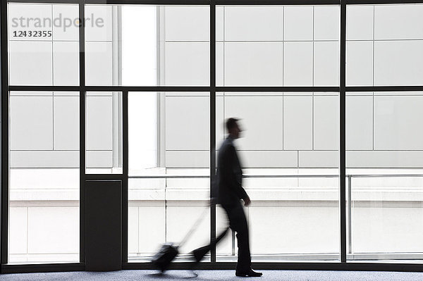 Ein Geschäftsmann verschwimmt in seiner Silhouette  während er an einem großen Fenster in der Lobby eines Kongresszentrums vorbeigeht.