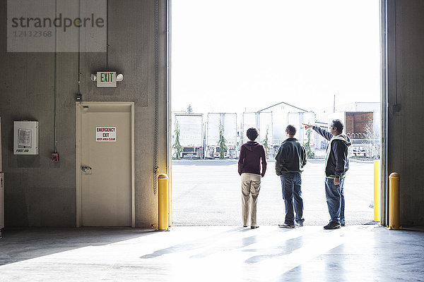 Drei Mitarbeiter warten auf eine Produktlieferung  während sie in einem Verladetor eines Auslieferungslagers stehen.