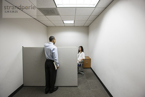 Ein schwarzer Geschäftsmann im Gespräch mit einer asiatischen Geschäftsfrau  die in einem kleinen Eckbüro arbeitet.