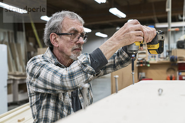 Leitender Zimmermann beim Bohren einer Schraube in einen Schrank in einer großen holzverarbeitenden Fabrik.
