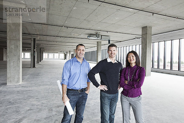 Ein Architekt und zwei Besitzer eines neuen rohen Geschäftsraums stehen in einer Reihe.