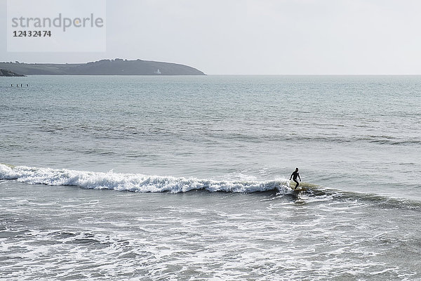 Surfer im Neoprenanzug reitet in Küstennähe auf der Meereswelle.