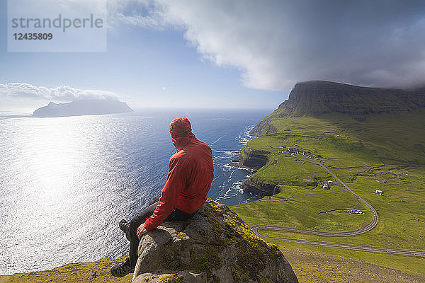 Wanderer sitzt auf Felsen und schaut auf das Meer  Gasadalur  Vagar Island  Färöer Inseln  Dänemark  Europa