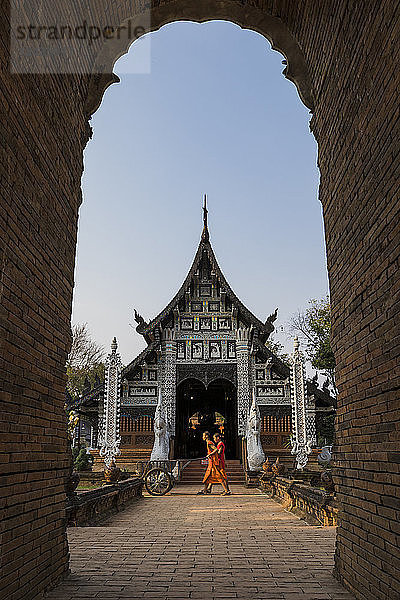 Tempel Wat Lok Moli durch einen Bogen gesehen mit zwei Mönchen im Vorbeigehen  Chiang Mai  Thailand  Südostasien  Asien