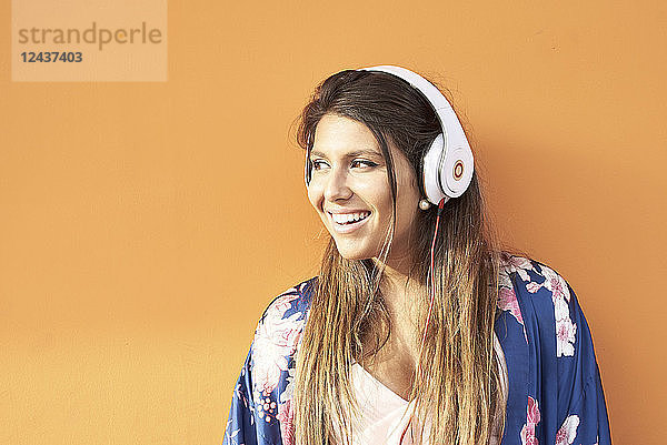 Portrait of smiling young woman with headphones in front of orange background