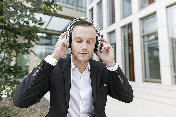 Young businessman with closed eyes wearing headphones outdoors