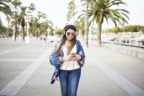 Portrait of woman wearing sunglasses listening music with headphones while looking at smartphone
