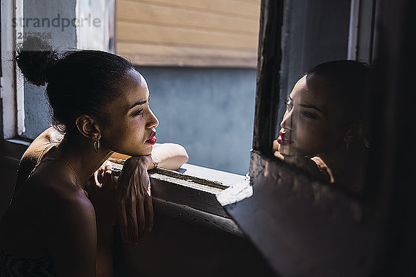 Beautiful young woman leaning on window frame reflected in mirror