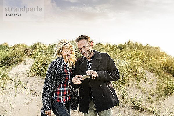 Happy couple in dunes sharing cell phone