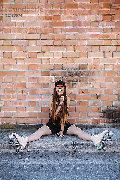 Portrait of laughing young woman with roller skates sitting on sidewalk