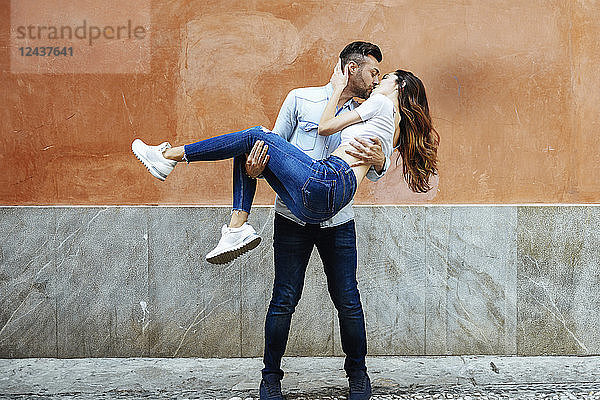 Carefree couple in love kissing in front of a wall outdoors