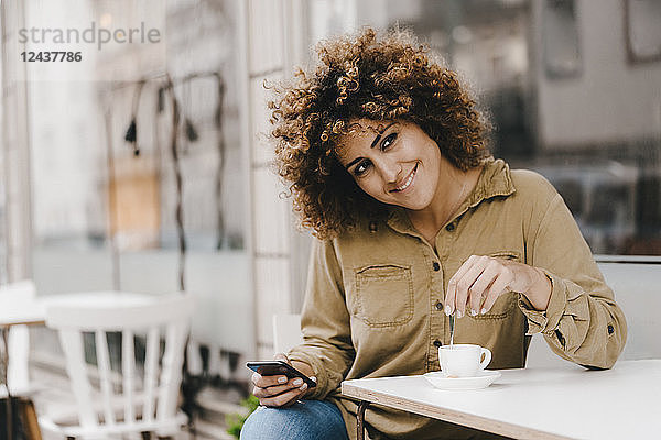 Woman in front of coffee shop  drinking coffee  holding smart phone