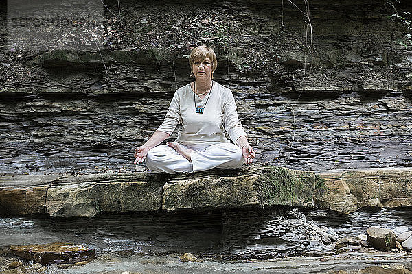 Senior woman doing yoga  meditating on rock