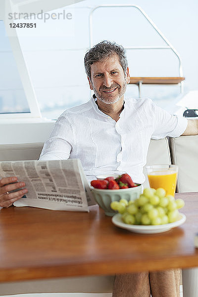 Mature man on a sailing trip having a healthy breakfast  reading newspaper