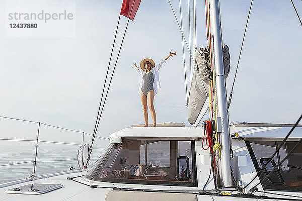 Mature woman standing on catamaran  waving with raised arms