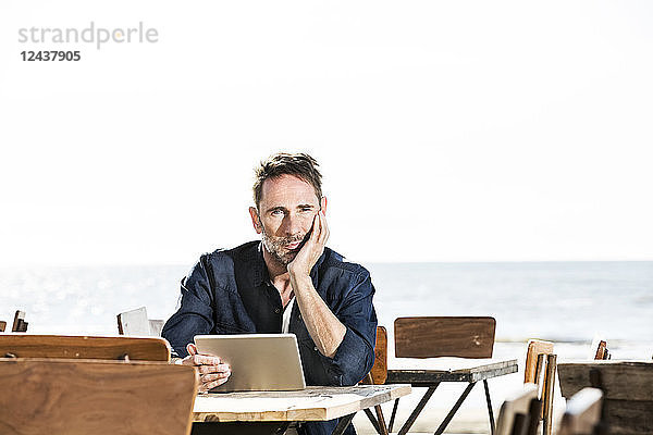 Man with tablet sitting in a cafe on the beach