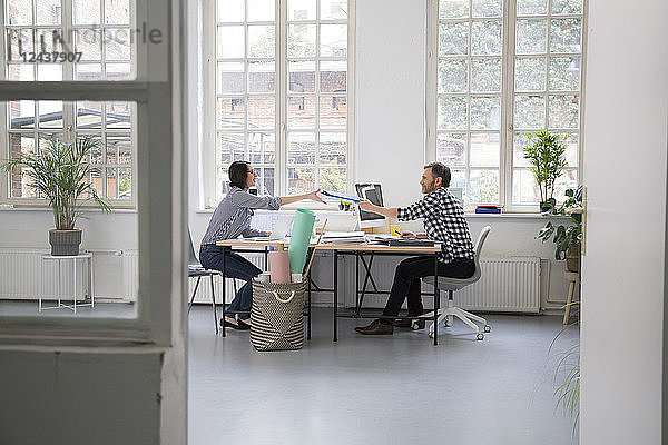 Man handing over folder to colleague at desk in a loft office