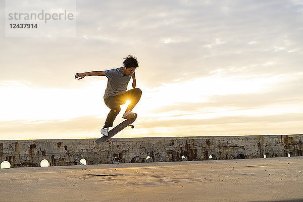 Young Chinese man skateboarding at sunsrise near the beach