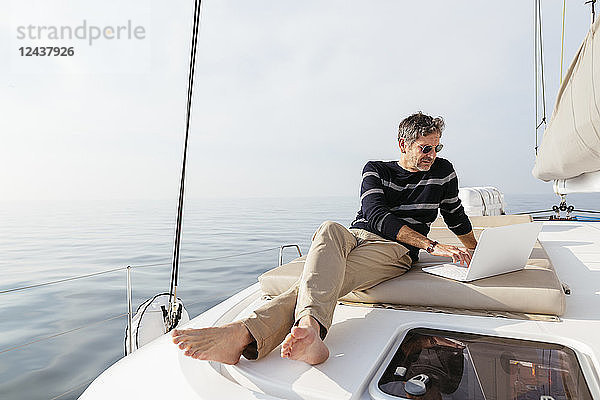Mature man sitting on deck of a catamaran  using laptop