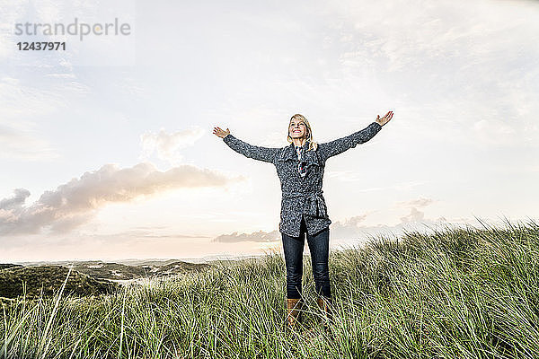 Happy woman standing in dunes with raised arms