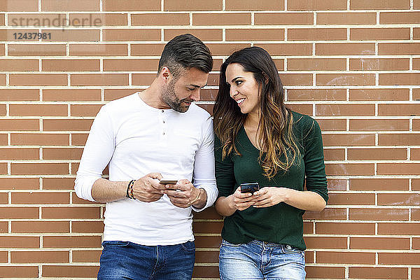 Couple looking at their smartphones at a brick wall