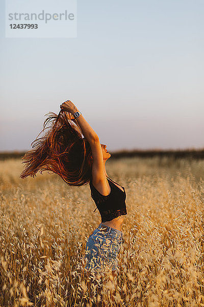 Young woman standing in grain field enjoying sunset