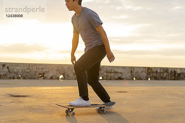 Young Chinese man skateboarding at sunsrise near the beach