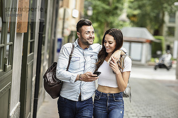 Smiling tourist couple with cell phone walking in the city