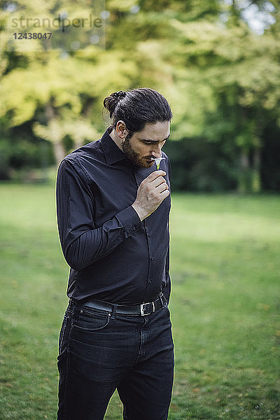 Young man  dressed in black  standing in park  smelling flower