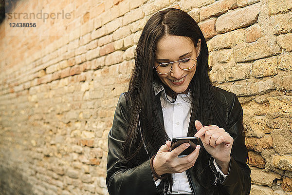 Smiling young woman using cell phone at brick wall