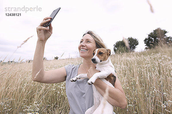 Woman with dog taking selfie with smartphone on a field