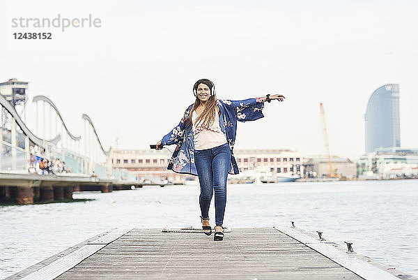 Spain  Barcelona  happy young woman with headphones dancing on jetty