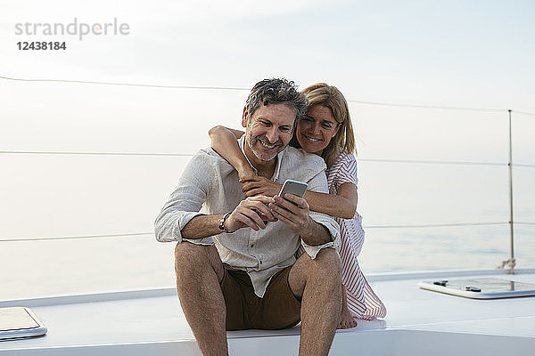 Mature couple looking at smartphone  sitting on a sailing boat
