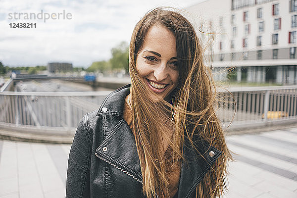 Portrait of smiling young woman with windswept hair on motorway bridge